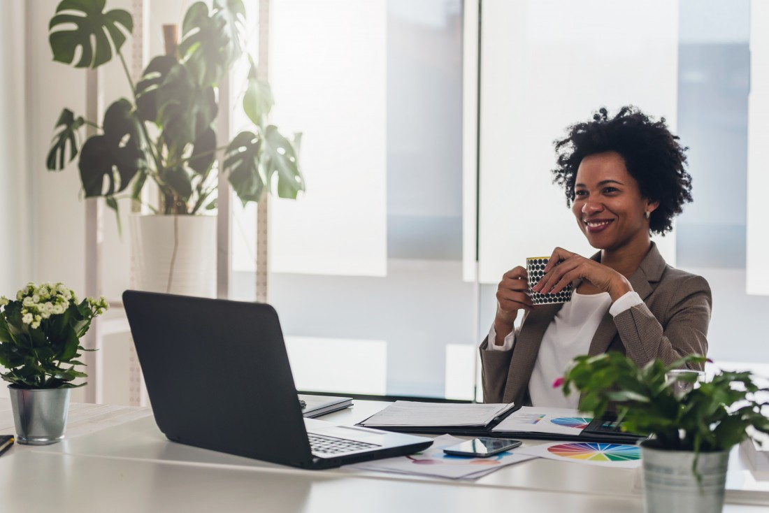 A woman enjoying coffee while working in a modern office, representing corporate housing services in Alabama by M2 Property Group